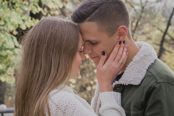 Couple in love stand on autumn fallen leaves in a park, enjoying a beautiful autumn day. Man hugs girl