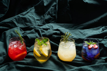 Multi colored assortment of herbal and fruit iced tea with citrus, berries and fruit syrups on deep dark turquoise cloth during studio shooting