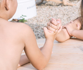 Little boy and girl sitting at table at summer beach and arm wrestling. Funny games for summer vacations.
