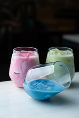 Side view of green, blue and pink matcha iced tea in glasses on dark blurred background