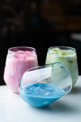 Side view of green, blue and pink matcha iced tea in glasses on dark blurred background