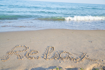 relax word is written on the beach sand