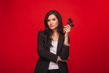 Girl holding makeup brushes on red background