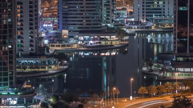 Jumeirah Lake Towers residential district aerial night timelapse near Dubai Marina. Illuminated modern skyscrapers reflected in water and traffic from above
