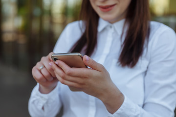 Portrait young business woman wearing white shirt using smartphone out doors. Female reading sms message in working process.