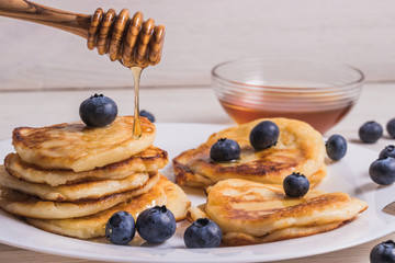 Cheesecakes on a plate with blueberries, in the background a plate with honey and a wooden spoon for honey.