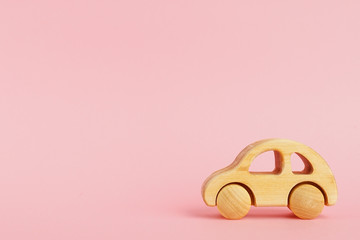 Wooden baby car on a pink pastel background with copyspace.
