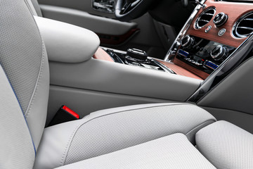 Modern luxury car white leather interior with natural wood panel. Part of leather car seat details with stitching. Interior of prestige modern car. White perforated leather. Car detailing. Car inside