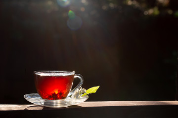 A cup of tea stands on a wooden table. Sun rays and bokeh. Dark background. Sunny summer evening, sunset.