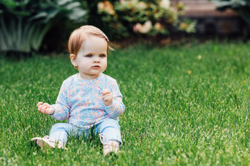 Outdoor portrait of a cute little girl in pretty wear siting on the garden grass.