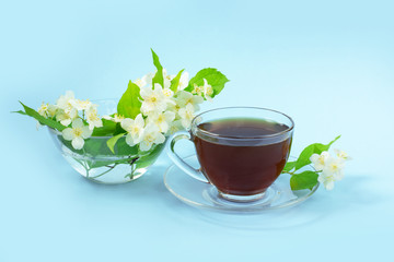 Cup with tea on a blue background. A small bouquet of twigs of blooming jasmine.