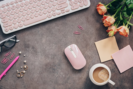 Flat lay female workspace - modern keyboard, mouse, cup of coffee, rose flowers, jewelry and stationery on a dark rustic background. Feminine office table desk frame. Top view