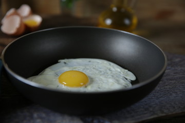Close-up. Frying pan with frying egg with yolk on a wooden cutting board with ingredients for the preparation of fried eggs: raw eggs, olive oil, salt. 