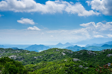Montenegro, Green hilly nature landscape of tree covered mountains and hills surrounding skadar lake water under blue sky in summer