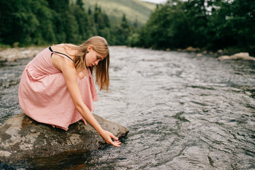Young lonely girl sitting at stone in the river.