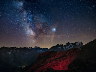 Naklejka premium Milky Way and starry sky on the Alps, Massif des Ecrins, Briancon Serre Chevalier ski resort, France. Panoramic view high mountain range and glaciers, astro photography, stargazing. Planet Jupiter