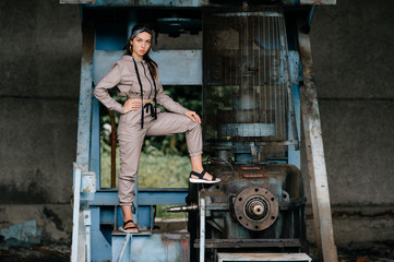 Beautiful young stylish girl posing at abandoned factory outdoor with an old broken engine.