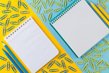 Paper clips and Notepad on bright yellow and blue paper background.