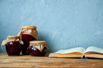 Three jars of jam and a recipe book on a wooden table