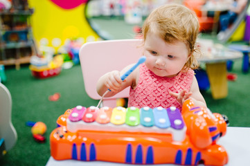 Fototapeta na wymiar Happy little kid, baby girl 1-2 years plays a musical instrument xylophone in game center, amusement of the children's room for birthday. indoor entertainment.