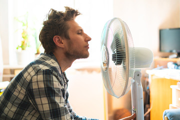 person enjoying the electric fan, cooling his face at home, during summer heat