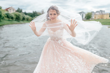 Beautiful  bride in wedding dress with veil over her face posing outdoor with lake on background.