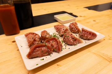 Two bottles of soy sauce and hot chili with red meat, shrimps and mushroom dumplings on a wooden table in an asian restaurant or chinese bar with dumplings.