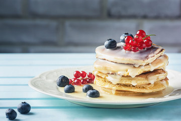 Fresh pancakes are sprinkled with condensed milk and decorated with blueberries and currants. Tasty and healthy dessert close-up. Bright photo.