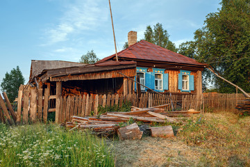 Village street in summer. Rickety wooden farmhouse with pile of firewood in front of it. Village of Visim, Sverdlovsk region, Urals, Russia