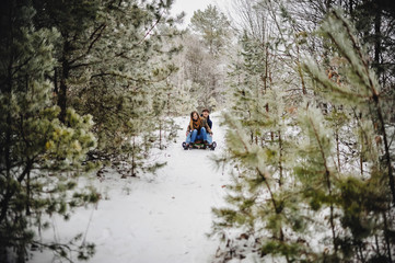 Obraz premium Smiling and happy couple enjoy in sledding on downhill in a forest or city park. Two young people sliding on a wooden sled at snow winter day.