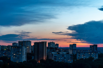 Before us the setting sun barely illuminates the high-rise buildings of one of the districts of Perm. Forest visible in the distance. Late evening, summer, July.