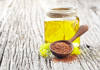 Camelina oil with sedds and flowers on wooden background