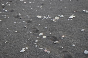 foot prints on a black sand with rocks beach 
