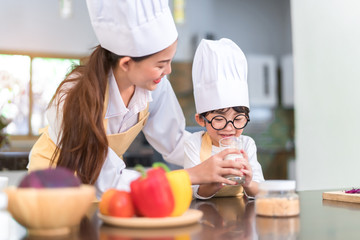 Happy family asian mom helping little son drinking milk for healthy in the kitchen room at home lifestyle.