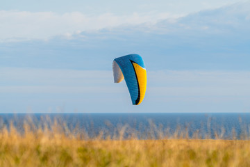 A colourful paraglider in the air with the sea as a backdrop
