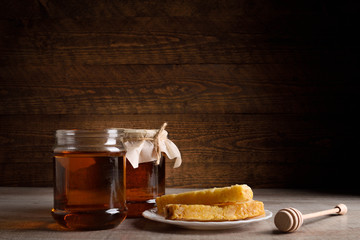 Honey in cans as well as honeycomb sots a wooden spoon on a wooden background