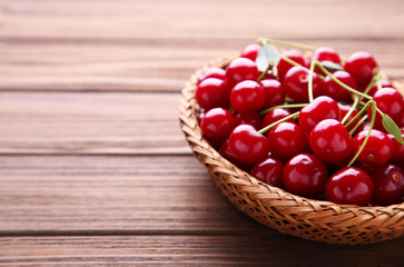Cherry in wooden basket with leaves on brown table.