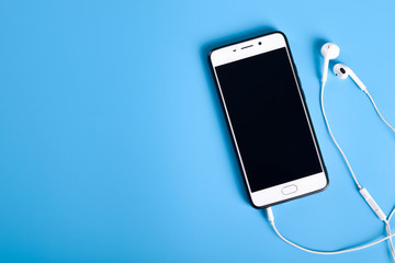  Mobile headphones and a mobile phone of white color on a blue background in light colors with a...