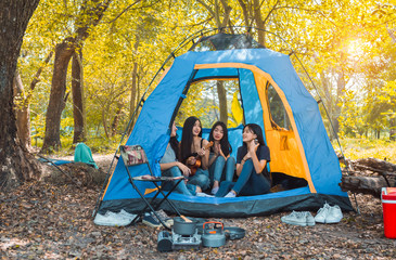 Friends Group of Young Asian women camping and resting at forest playing ukulele,take a photo happy in the tent cooking picnic people travel lifestyle.