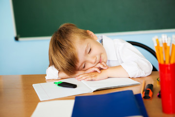 The boy primary school student is tired and sleeps at the desk. Difficult school assignments. Overwork.