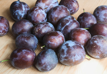 A lot of ripe plums on a wooden table, space