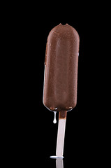 cream ice cream with chocolate icing on a wooden stick on a black background with a reflection