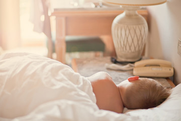 Rear view shot of a kid sleeping on a bed under the white blanket.