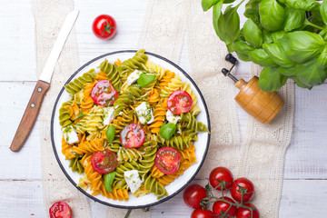 Italian food - Salad with colorful pasta, cherry tomatoes, feta cheese and fresh basil on white wooden background