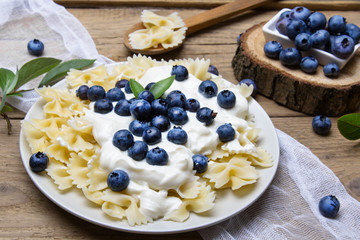 Tasty pasta with fresh organic blueberries and vanilla cream. Sweet dinner on retro wooden table.