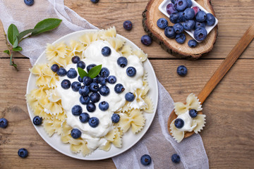 Tasty pasta with fresh organic blueberries and vanilla cream. Sweet dinner on retro wooden table.