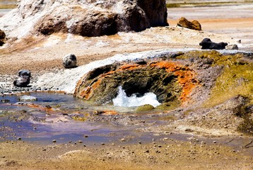 Close up of geyser hole with hot bubbling boiling water and rusty reddish edge in dry barren arid...