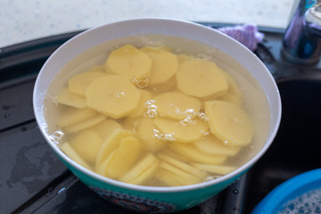Sliced potatoes in water in a metal bowl