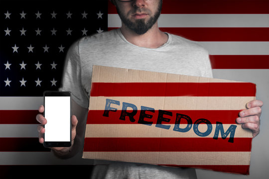 Concept of freedoms and human rights. A man with a cardboard and a phone in his hand. The Flag of USA. Text freedom and mck up