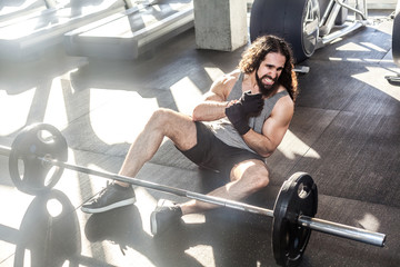 Portrait of screaming young adult man athlete with long curly hair working out in gym, sitting on...